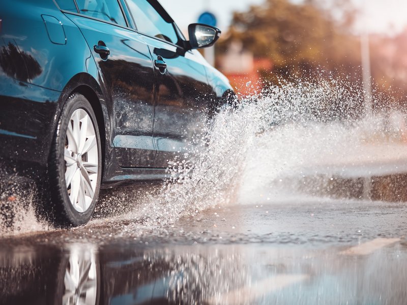 Aquaplaning und Wasserwelle bei Starkregen Schwarzes Auto fährt durch eine nasse Senke und erzeugt eine große Wasserwelle.